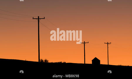 Bauernhof Gebäude und Maschinen unter elektrischen Leitungen im Morgengrauen in der Nähe von vier Ecken im östlichen Wyoming. Stockfoto