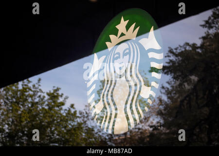 Blick auf die Beschilderung von berühmten, internationalen Coffee-Shop-Kette und Reflexionen von Bäumen auf einer Glasoberfläche. Stockfoto