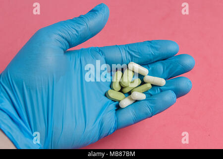 Sortiment von Pillen, Tabletten und Kapseln auf Hand in Blau Handschuh gegen Rosa Hintergrund. Stockfoto