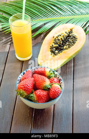 In der Hälfte reife Papaya frische Erdbeeren tropischen Saft in hohes Glas mit Stroh Palm Leaf auf der Plank Holz Tisch im Café. Urlaub Sommer Reisen Rela Stockfoto