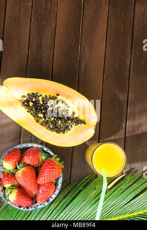 In der Hälfte reife Papaya frische Erdbeeren tropischen Saft in hohes Glas mit Stroh Palm Leaf auf der Plank Holz Tisch im Café. Urlaub Sommer Reisen Rela Stockfoto