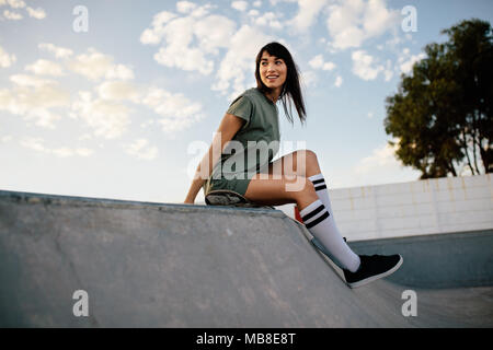 Weiblichen skateboarder sitzen auf einer Rampe im Skate Park. Frau eine Pause nach Skateboarding im Park. Stockfoto