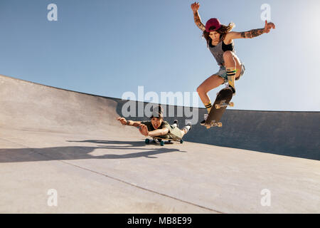 Zwei Frauen, die Stunts auf Skateboards bei Skate Park. Weibliche Freunde üben Skateboarding im Freien. Stockfoto