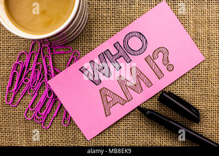 Handschrift Text schreiben Wer bin ich Frage. Begriff Sinne Frage Identität denken Zweifel Psycology Geheimnis auf Rosa Zettel Papier auf das Jute Hintergrund Kaffee Tasse Kugelschreiber Pins geschrieben. Stockfoto