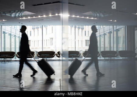 Motion Schuß in der zuversichtlichen Unternehmer ziehen Koffer beim Gehen entlang geräumigen Warteraum der moderne Internationale Flughafen Stockfoto