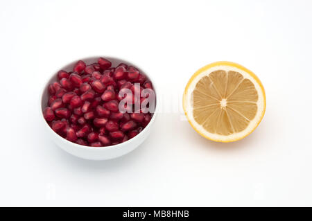 Gelbe frische Zitronen auf weißem Hintergrund, Samen von Granatäpfeln in eine Tasse. Stockfoto