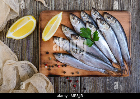 Eine kleine gesalzene Hamsa (Sprotte) mit Gewürzen, Zitrone auf einem Holz- Hintergrund. Ansicht von oben. Stockfoto