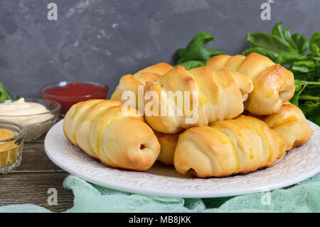 Weiche hausgemachten Brötchen mit Wurst auf einem weißen Keramik Teller mit verschiedenen Saucen. Würstchen im Teig. Stockfoto