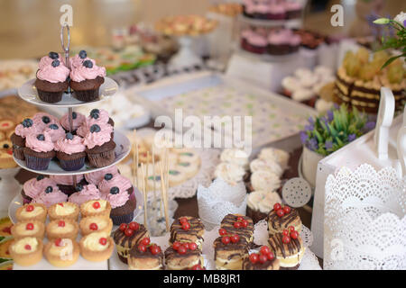 Leckere Muffins mit Beeren auf einem mehrstufigen Kuchen und eine große Auswahl an Süßigkeiten und Kuchen an einem candy Buffet für eine feierliche Veranstaltung gesorgt Stockfoto