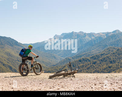 Foto von Mann in Helm auf dem Fahrrad auf der Straße gegen den Hintergrund der Berge und blauer Himmel Stockfoto