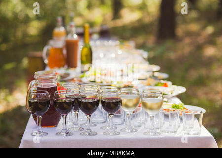 Catering für draußen Party oder Picknick. Detailansicht Brille mit roten und weißen Wein und verschwommen Vorspeisen auf Platten im Hintergrund. Tisch serviert in Stockfoto