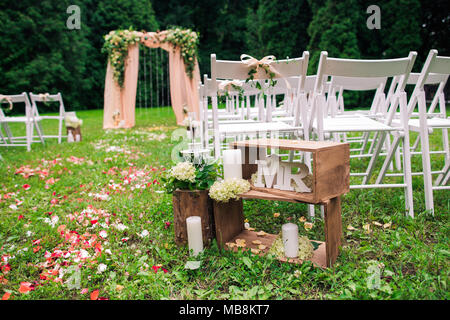 Wunderschöner Ort mit Holz- und Blumen Rosen Dekorationen für außerhalb der Trauung im Green Park gemacht. Reihen von viele leere Stühle aus Holz lesen Stockfoto