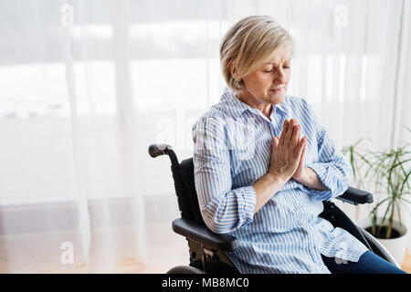 Eine ältere Frau im Rollstuhl zu Hause beten. Stockfoto