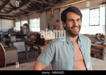 Lächelnd woodworker stützte sich auf eine Tabelle in der Holzbearbeitung studio Stockfoto