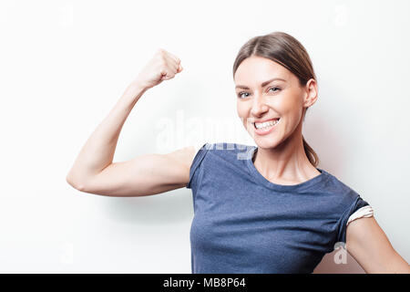 Schöne junge Frau in Blau shirt posiert mit erhobenen Armen. Porträt von Brust studio Schuß auf Teal Hintergrund. Stockfoto