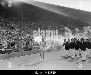 Olympischen Spiele, London, 1948. Britische Athleten John Mark bringt die olympische Fackel rund um die Strecke und schließlich leuchtet die Olympische Flamme. Stockfoto