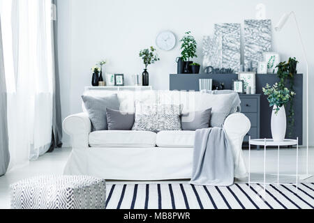 Gemütliche weiß Sofa und einem gestreiften Teppich in ein stilvolles, modernes Wohnzimmer Interieur mit grauen Möbeln und Dekorationen Stockfoto