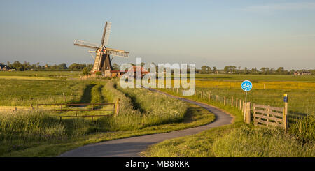 Holländische Windmühle aus Holz mit kleinen Miller Haus und Radweg bei Sonnenuntergang im Sommer mit Blumen Stockfoto