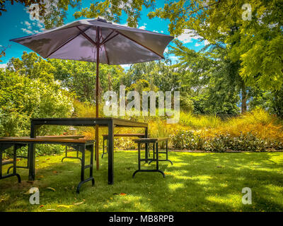 MARLBOROUGH, NEUSEELAND - 6. Dezember: Möbel Esstisch mit Stühlen und Sonnenschirm im Schatten in einem üppigen Garten im Hinterhof Stockfoto