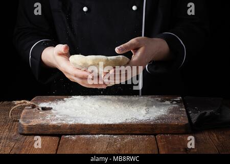 Köchin holding Hefeteig in ihren Händen auf schwarzem Hintergrund Stockfoto