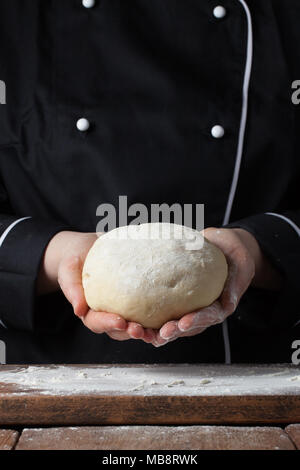 Köchin holding Hefeteig in ihren Händen auf schwarzem Hintergrund Stockfoto