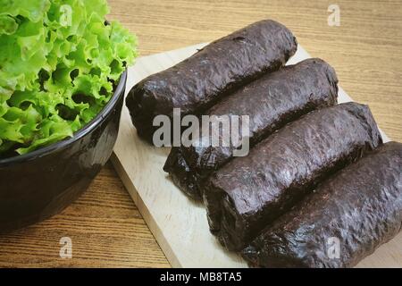 Japanische Küche, Traditionelle ungeschnitten Japanischen Reis Maki Sushi Roll mit Nori Algen auf Schneidebrett serviert mit grünen Eichen. Stockfoto