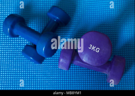 Neopren beschichteten Bügeleisen, ein paar Hanteln von 3 kg und ein Paar 2 kg, für Muskelaufbau, Aerobic- und, auf eine blaue Matte positioniert Stockfoto