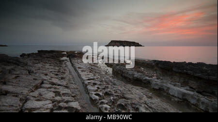 Felsige Küstenlandschaft bei dramatischen Sonnenuntergang mit der kleinen Insel Geronisos st. Georges Cape in Paphos Bereich Halbinsel Akamas in Zypern Stockfoto