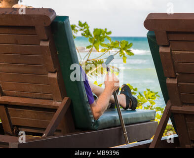 Ein alter Western Mann mit einem Stock, Sitzen auf einem Liegestuhl und genießt seinen Ruhestand im Ausland. Im Februar 2018 in Terengganu, Malaysia übernommen. Stockfoto