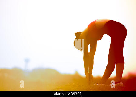 Gesunde Frau stretching Kniesehne Muskel für Aufwärmen oder Abkühlen, Muskel stretching Übung für verhindern Verletzungen der Muskulatur nach dem Training, Silhouetted w Stockfoto