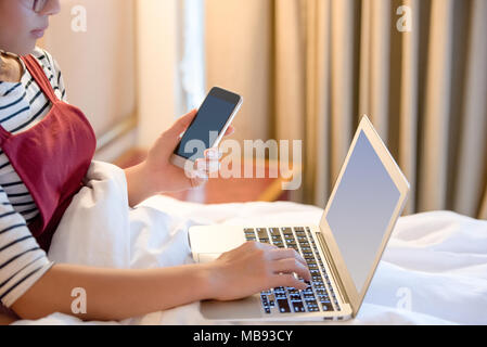 Die Frau, die zu Hause arbeiten, der Rest der Zeit zu Hause arbeiten oder home business, Frau mit Laptop und legte die Hand auf Laptop Tastatur und Holding smart Pho Stockfoto