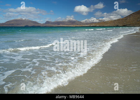 Wellen auf den menschenleeren Strand bei Luskentire auf der Isle of Harris im Frühling mit Schnee auf den Hügeln im Hintergrund. Stockfoto