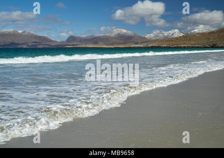 Wellen auf den menschenleeren Strand bei Luskentire auf der Isle of Harris im Frühling mit Schnee auf den Hügeln im Hintergrund. Stockfoto