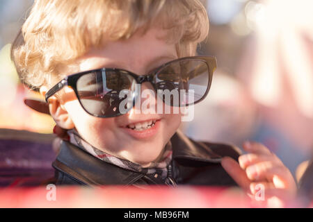 Wunderschöne Babys, blonde Haare mit großen schwarzen Brille lächelnd in die Kamera, Tageslicht mit Flares, bis Portrait schließen. Stockfoto