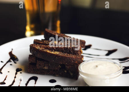 Würzigen Roggen Cracker mit Knoblauch Sauce mayonnaise Snacks auf weiße Platte und Bier auf schwarz Tisch in der Bar Stockfoto