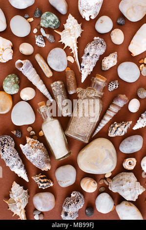 Muster der Sand in den Glasflaschen, Muscheln und Steinen auf dem braunen Papier Hintergrund, flach Stockfoto