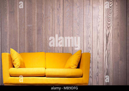 Gelbe Sofa vor eine Holzwand mit Kopie Raum Hintergrund. Stockfoto