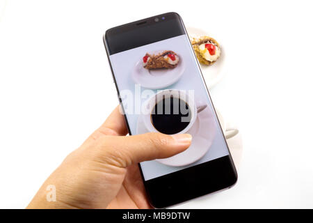 Close-up-Bild. die Hände sie ihr Smartphone ein Foto von Kaffee und süßes Dessert in weißen Hintergrund zu nehmen. Stockfoto