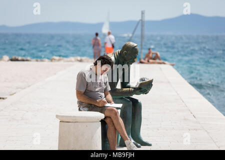 Mann schreiben in einem Notebook sitzen neben der Statue eines Wissenschaftlers an einer Shell anstarren, Hafen von Zadar, Kroatien Stockfoto