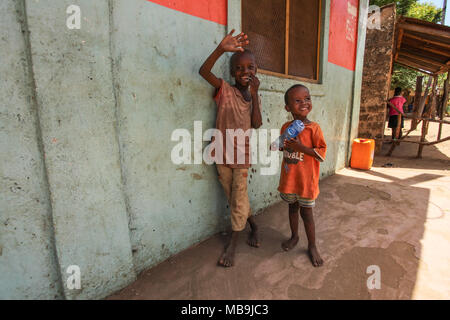 Malindi, Kenia - April 06, 2015: Zwei unbekannte kleine Jungen, neben Wand, lächelnd und winkend auf die touristischen Besuch der lokalen Slum. Viele Kinder suff Stockfoto