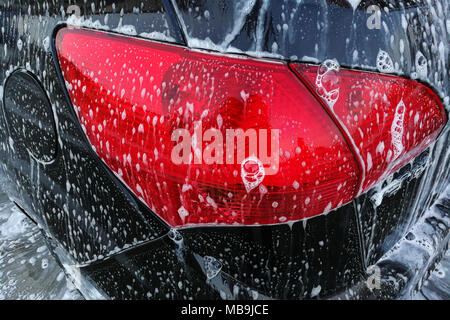 Detail Foto von Braun Auto hinten rotes Licht mit Seife Schaum abgedeckt, wenn in der Waschhalle gereinigt wird. Stockfoto