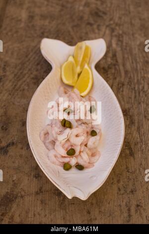 Meeresfrüchte Konzept. Rohe Garnelen mit Zitrone und Kapern in einem Fisch geformte keramische Platte. Vertikale Rahmen. Stockfoto