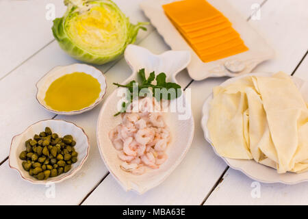 Zutaten für Blätterteig mit Garnelen, Olivenöl, dünne Fladenbrot Blätter, Kapern und Käse auf weißem Holz- Tischplatte Stockfoto