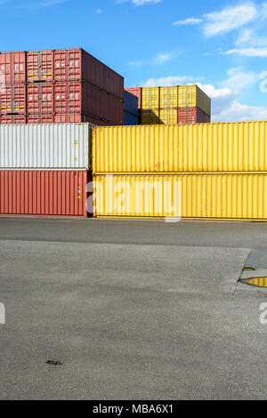 Dry Cargo Container in verschiedenen Farben in einem Yard unter einem blauen Himmel mit weißen Wolken gestapelt. Stockfoto