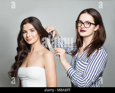 Friseur oder Frisör mit Lockenstab für perfekte Locken. Frisur und Friseursalons. Frau, die Locken auf lange braune Haare. Abends Frisur mit R Stockfoto