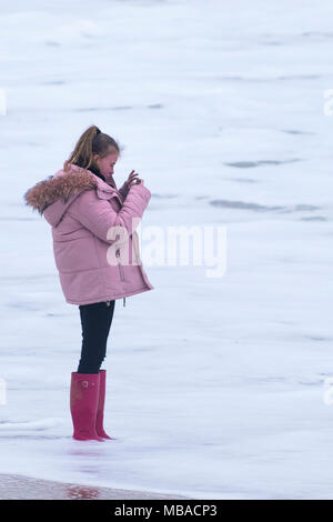 Ein junger Teenager tragen rote Gummistiefel und stehen im Meer. Stockfoto