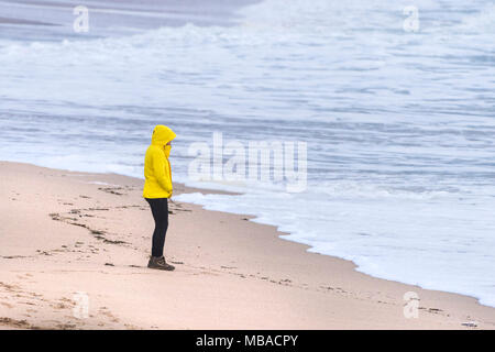 UK Wetter. Eine Frau trägt eine helle gelbe Jacke Braving das kühle Wetter an der Küste in Newquay Cornwall. Stockfoto