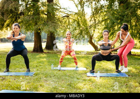 Schöne Freundinnen tun hockt Übung im Park mit weiblichen Fitness Trainer. Stockfoto