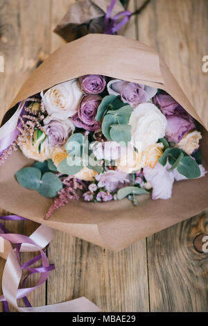Schönen frischen Blumenstrauß mit Eukalyptus, Rosen, Englische Rosen im Handwerk Papier verpackt auf dem alten Holztisch Hintergrund Stockfoto