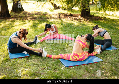 Vier schöne motivierte weibliche Freunde tun stretching Übung im City Park. Stockfoto